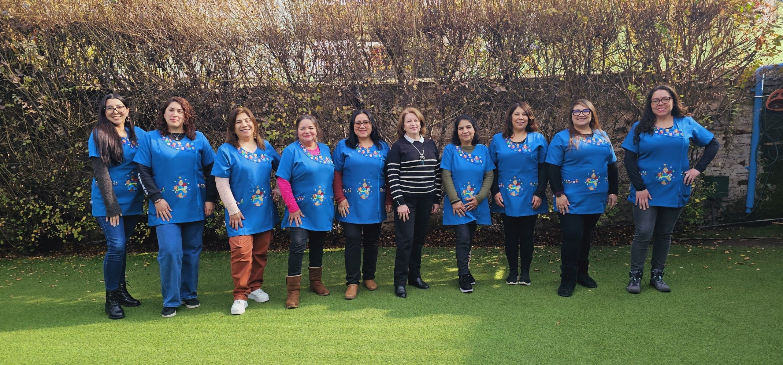 Equipo docente y directivo de Kineret, de pie en el patio del colegio con sus delantales azules.