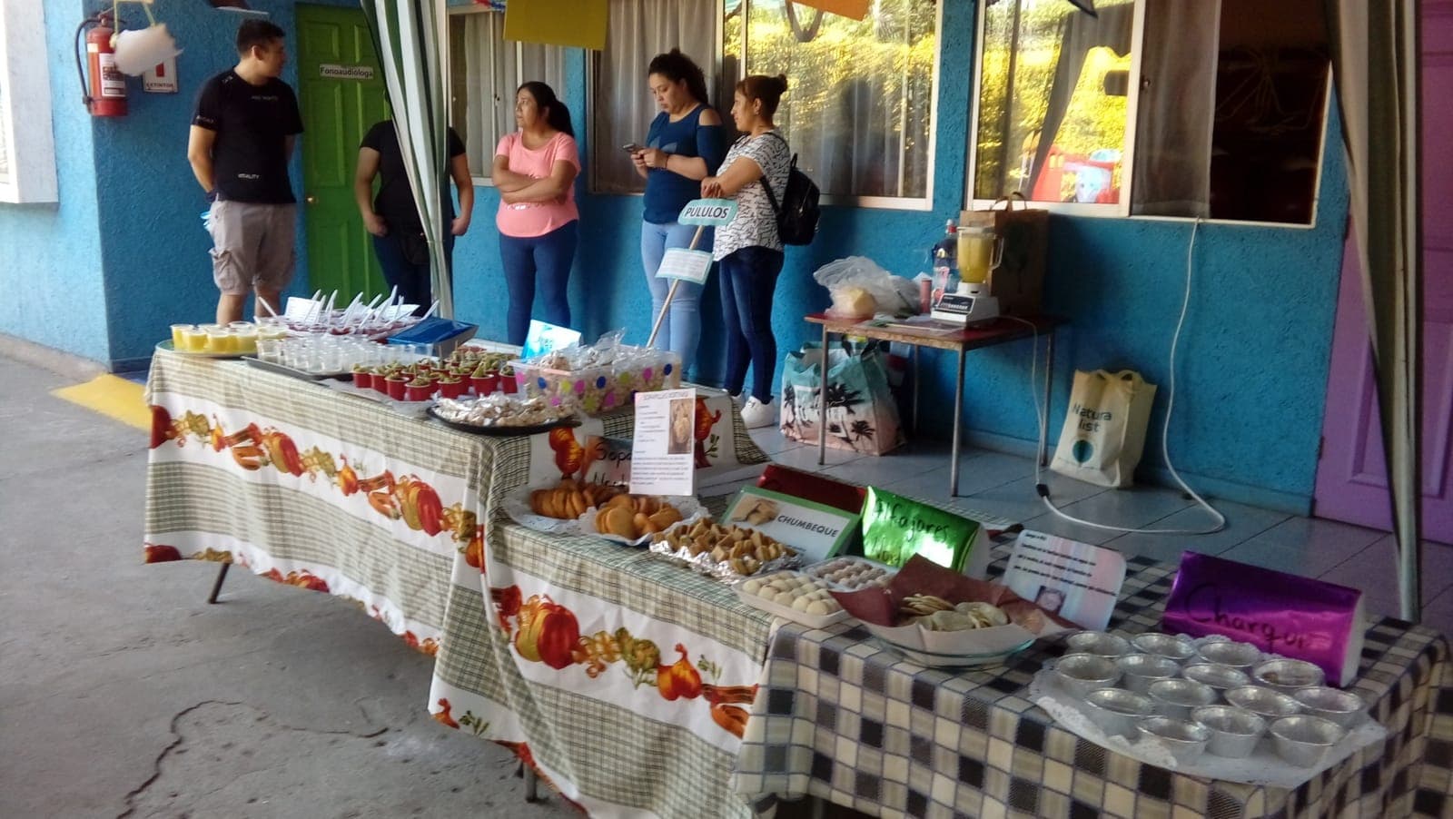 Familias junto a mesas con sopaipillas, alfajores, chumbeque y otras preparaciones en el patio del colegio.