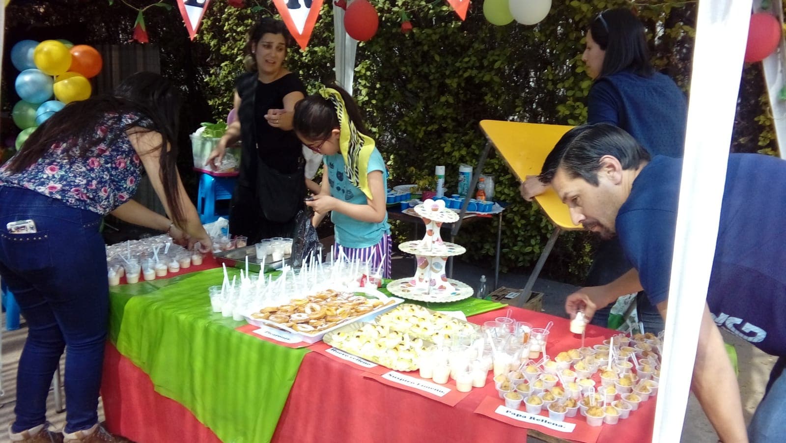 Apoderados y una niña ordenan una mesa con picarones, huevos rellenos, suspiro limeño y papas rellenas.