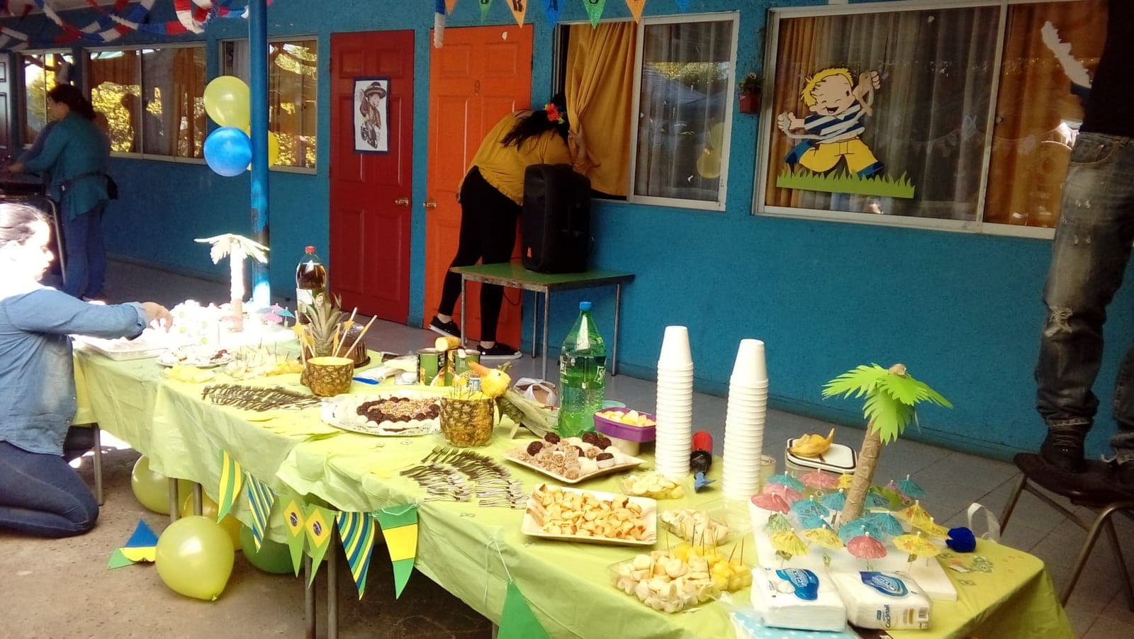 Mesa decorada con los colores de Brasil, con frutas, dulces y palmeras de papel.