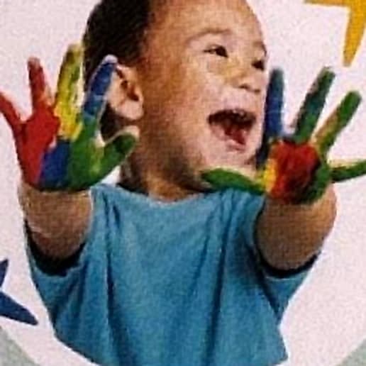 Niño riendo y mostrando sus manos pintadas de colores.